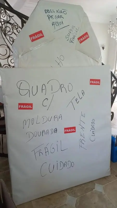 Quadro com moldura dourada embalado com proteção e etiquetas de frágil